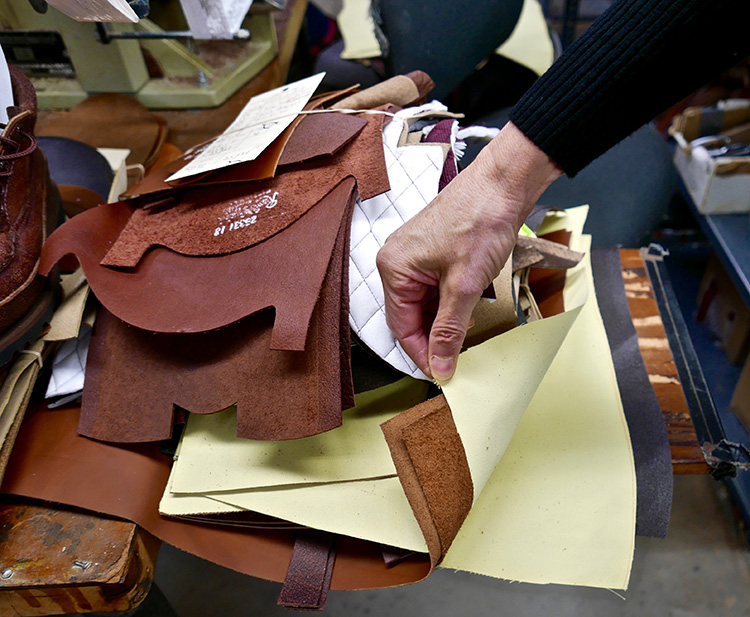 <p>The upper assembly station where the quarters are stitched to the vamp; backstays, collars and eyelet facings are all attached and stitched into place.  In this photo a pair of snake proof boots are to be assembled.  The off-white fabric is ‘Turtleskin.’ a Kevlar fabric which is impervious to snakebites.  Snake proof boots are popular in the southern United States where snakes are prevalent .<br />
甲の部分を縫い合わせるステーションでは、つま革に、かかと部分、カラー、アイレットの化粧面などが組み合わされ、縫い合わされます。この写真では、蛇から足を守るブーツが組み合わされています。オフホワイトの生地は、蛇にかまれても耐えられるケブラ生地の「タートルスキン」です。蛇の多いアメリカ南部では、防蛇のブーツが人気があります。</p>
