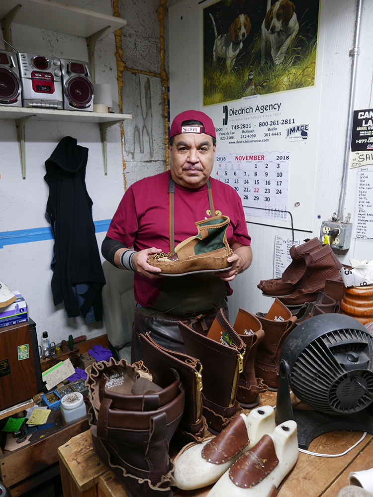 <p> Custom lasts in the foreground which have been built up by tacking leather, in this case,  to the insteps.<br />
The shoemaker is holding a boot with the vamps pulled up and tacked onto a custom last.<br />
この場合は、足の甲に合わせて、革を仮留めして、前面を組み立てているカスタムの木型。靴職人は、ブーツのつま革を引き伸ばして、カスタムの木型に合わせています。</p>
